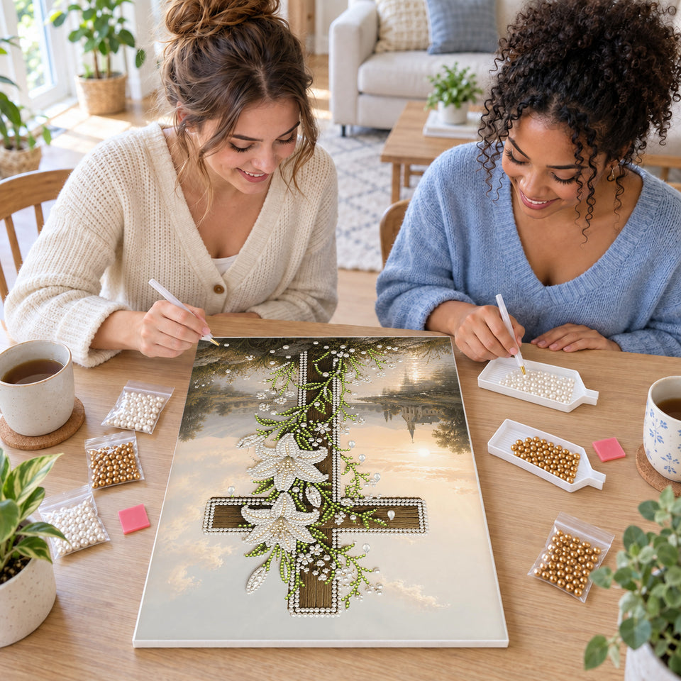 Two friends creating one shared Pearl artwork — Wooden Cross with White Lilies Beside a River. Pearl diamond painting DIY kit by Isuvio.