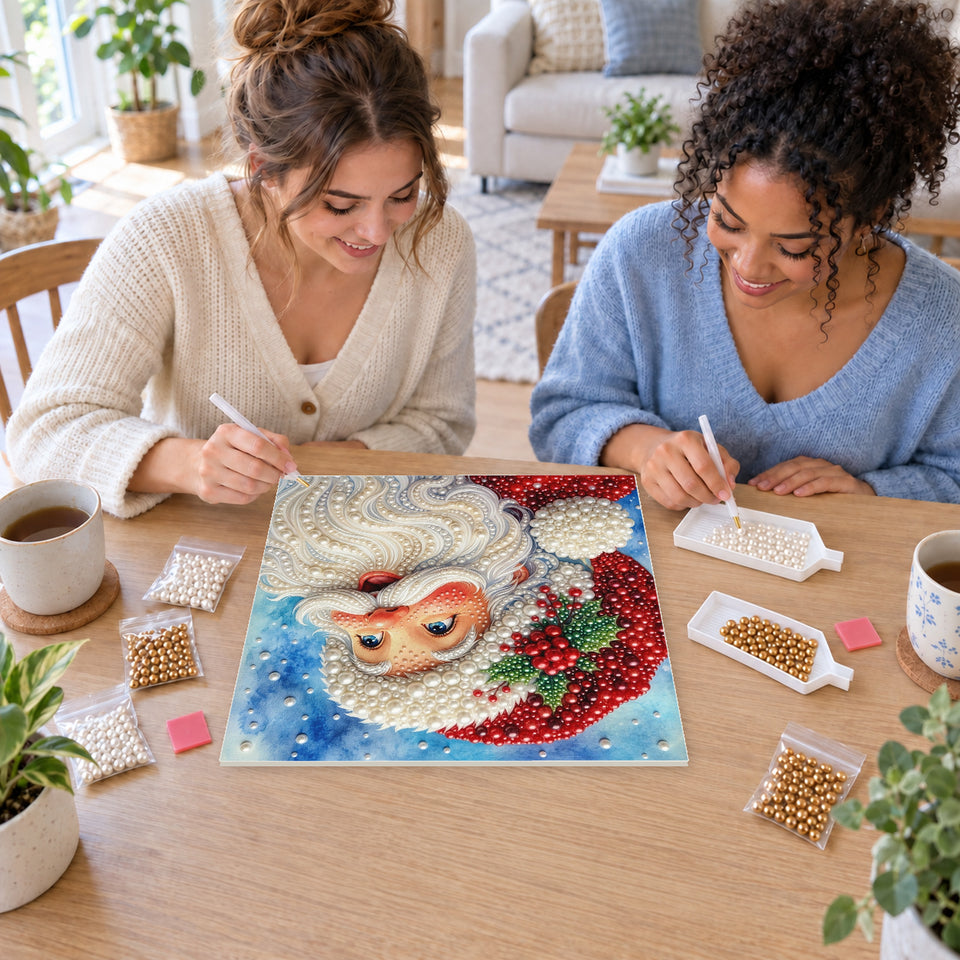 Two friends creating one shared Pearl artwork — Smiling Santa beneath a Snowy Blue Sky. Pearl diamond painting DIY kit by Isuvio.