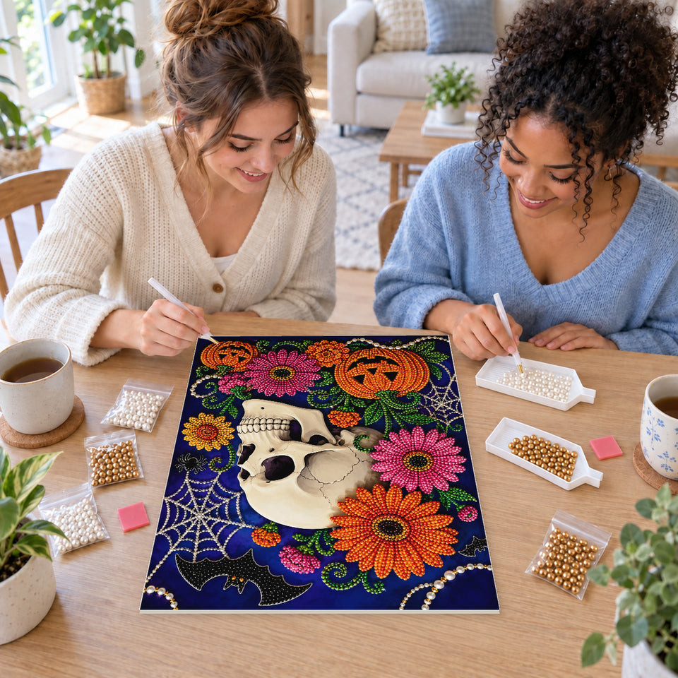 Two friends creating one shared Pearl artwork — Floral Skull with Pink Blossoms and Pumpkins. Pearl diamond painting DIY kit by Isuvio.