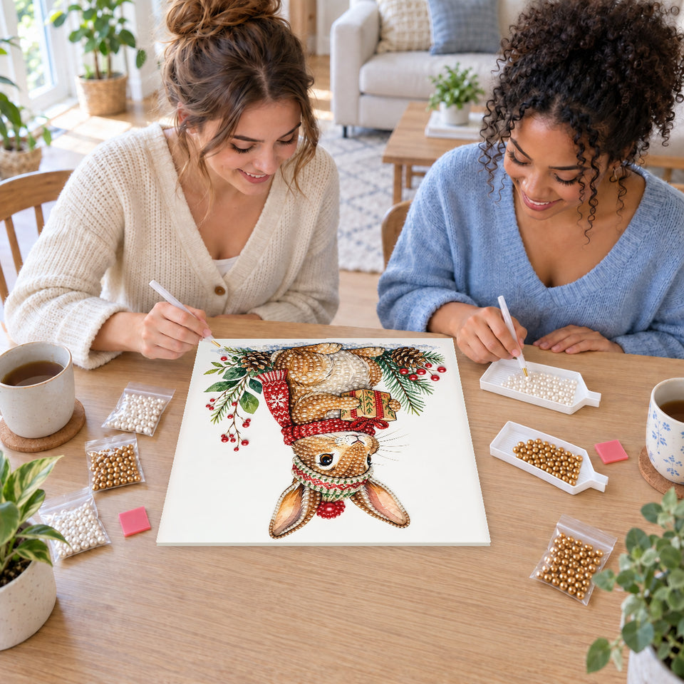 Two friends creating one shared Pearl artwork — Christmas Rabbit Carrying a Green Gift. Pearl diamond painting DIY kit by Isuvio.