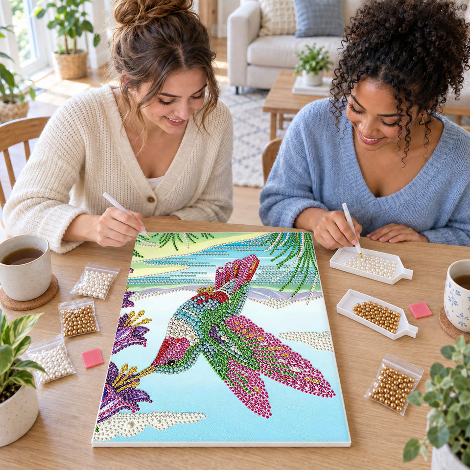 Two friends creating one shared Pearl artwork — Rainbow Hummingbird Beside Purple Flowers. Pearl diamond painting DIY kit by Isuvio.