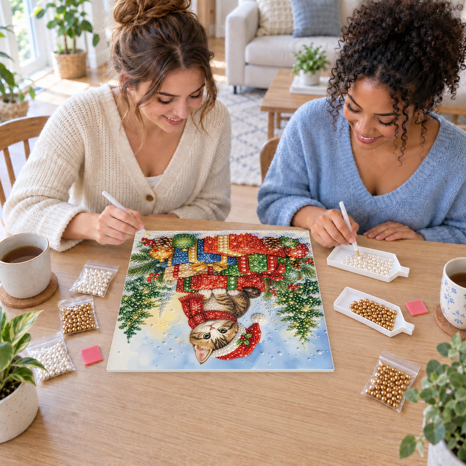 Two friends creating one shared Pearl artwork — Santa-Hat Kitten atop Christmas Presents. Pearl diamond painting DIY kit by Isuvio.