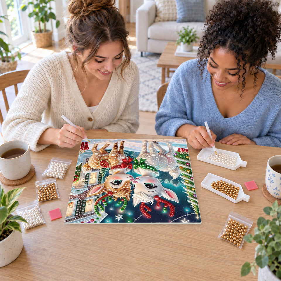 Two friends creating one shared Pearl artwork — Two Festive Fawns in a Snowy Village. Pearl diamond painting DIY kit by Isuvio.