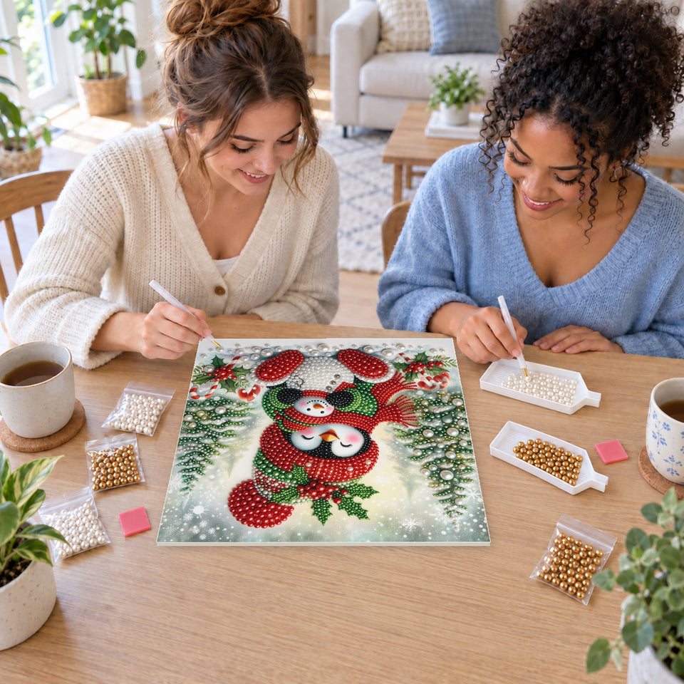 Two friends creating one shared Pearl artwork — Penguin Cuddling a Little Snowman at Christmas. Pearl diamond painting DIY kit by Isuvio.