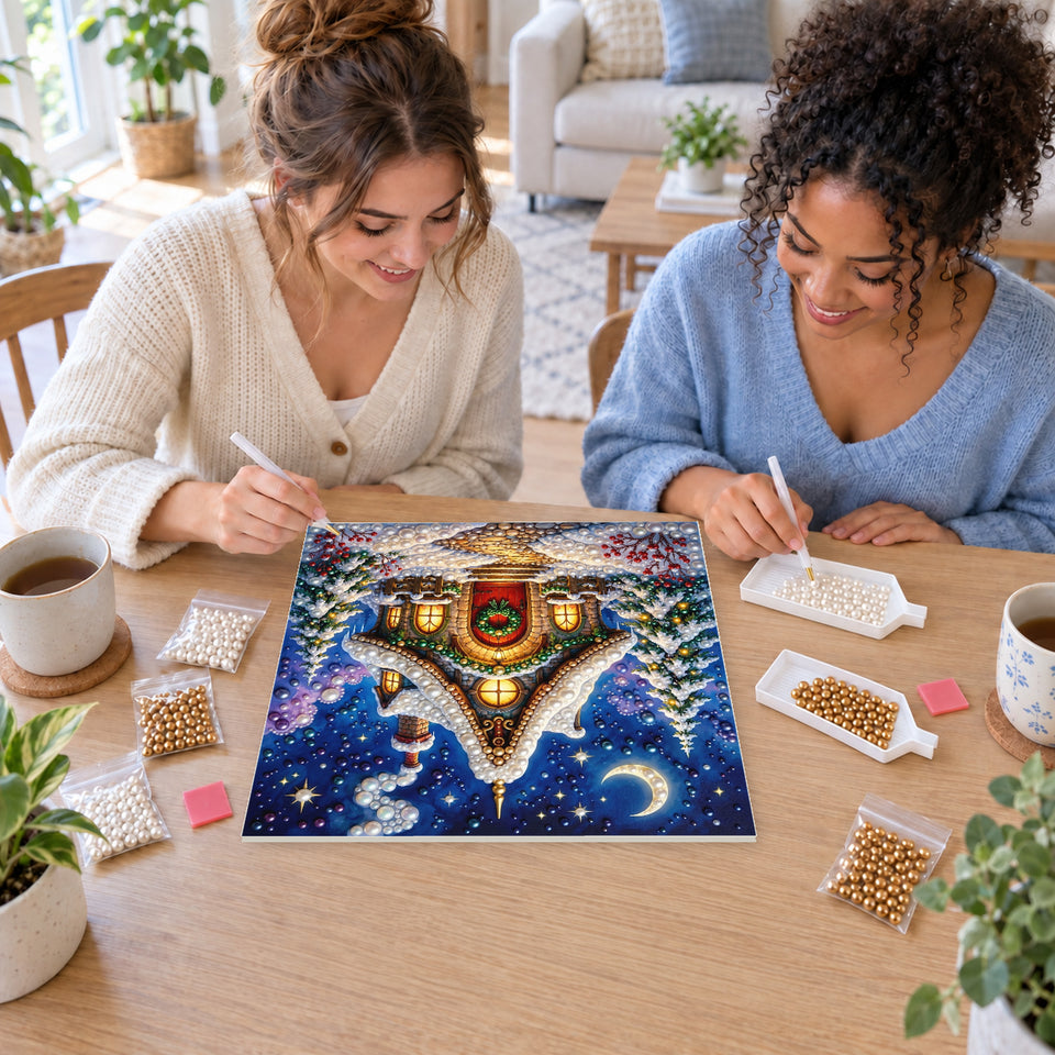 Two friends creating one shared Pearl artwork — Snowy Christmas Cottage beneath a Crescent Moon. Pearl diamond painting DIY kit by Isuvio.