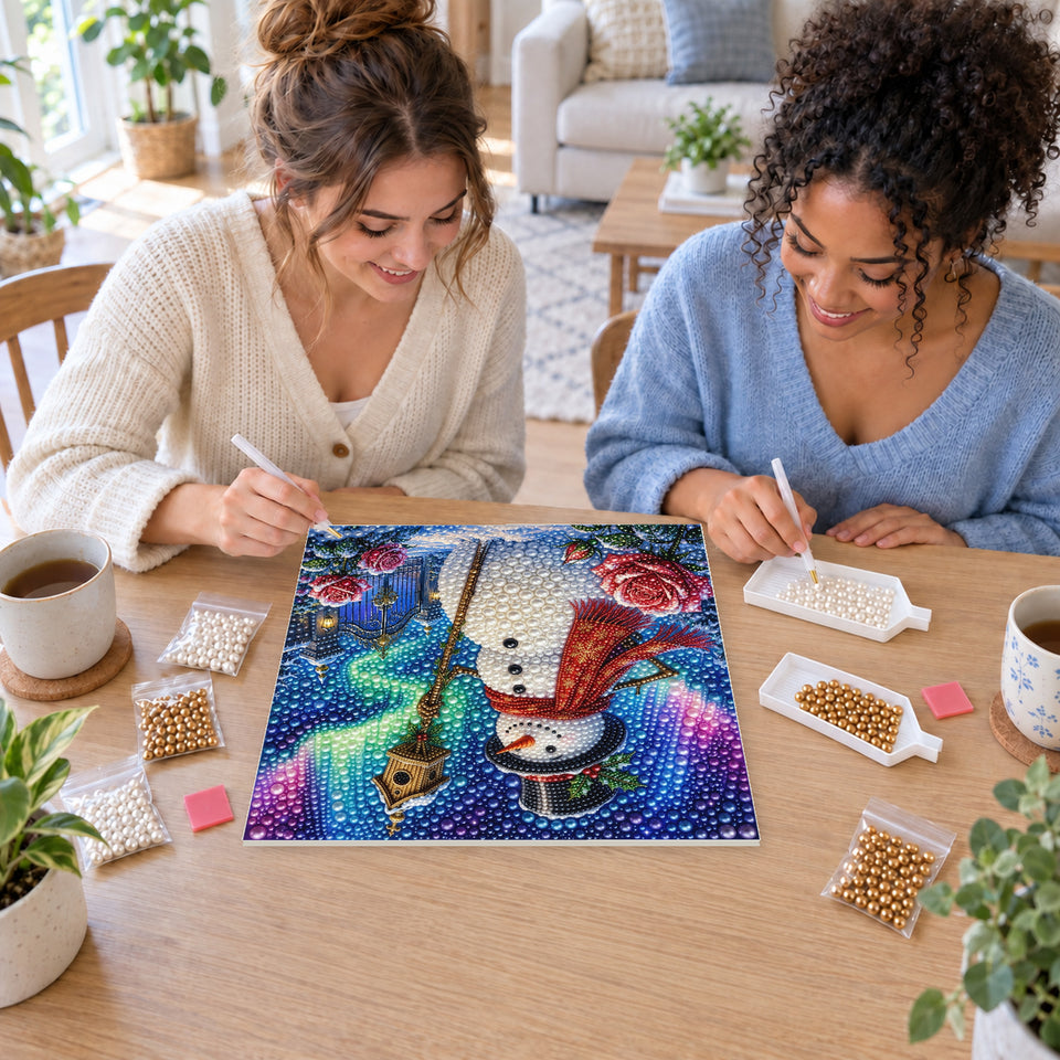Two friends creating one shared Pearl artwork — Snowman with a Birdhouse beneath the Aurora. Pearl diamond painting DIY kit by Isuvio.