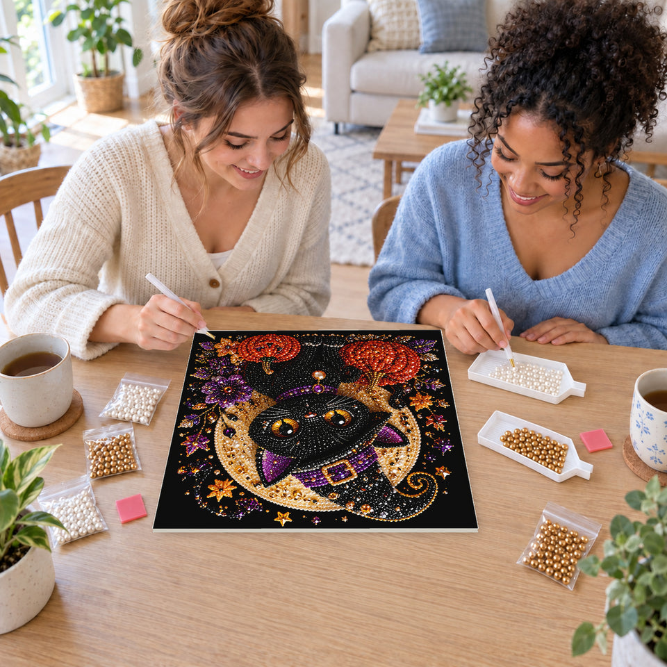Two friends creating one shared Pearl artwork — Black Witch Kitten beneath a Golden Moon. Pearl diamond painting DIY kit by Isuvio.