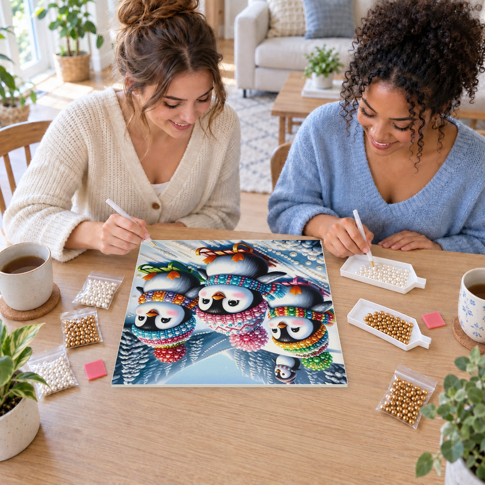 Two friends creating one shared Pearl artwork — Penguins Sledding Down a Snowy Mountain. Pearl diamond painting DIY kit by Isuvio.