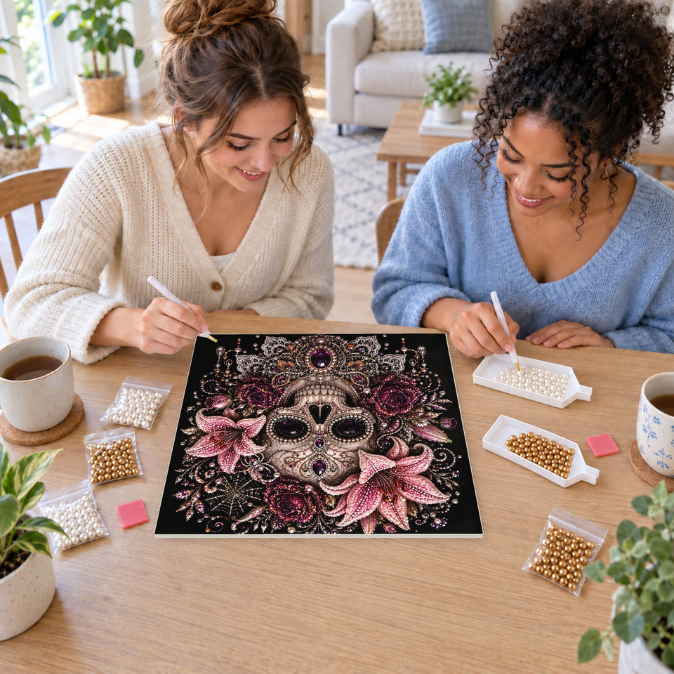 Two friends creating one shared Pearl artwork — Ornate Skull with Pink Lilies and Purple Jewels. Pearl diamond painting DIY kit by Isuvio.
